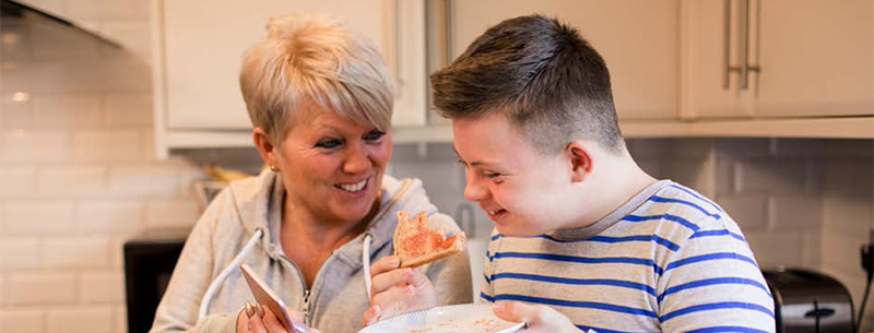 Mother smiles at teenage son as he eats toast