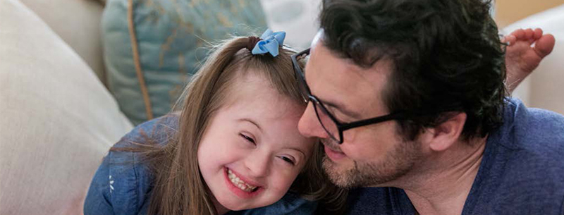 Father and daughter smile as they lean together on a couch