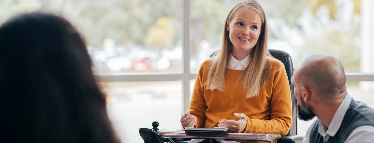 Woman in a wheel chair talking to a group in a meeting room