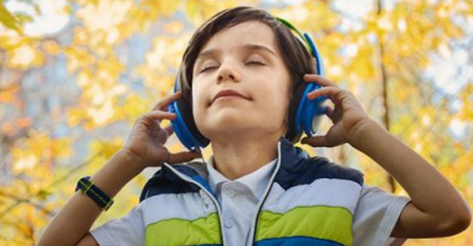 Young boy holding headphones over his ears with his eyes closed.