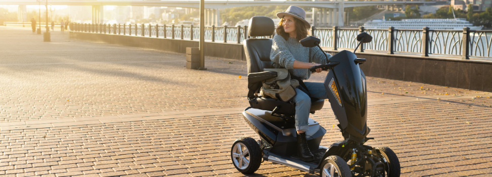 A lady drives her mobility scooter along an esplanade on a bright and beautiful day.