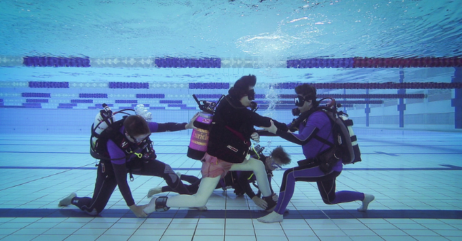 A participant in full scuba gear s doing therapy underwater with 3 assistants also in full scuba gear.