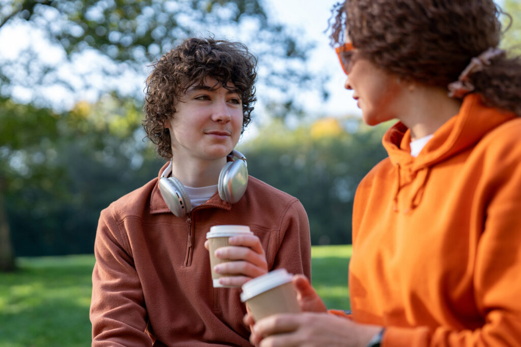Two people sitting in a park drinking coffee.