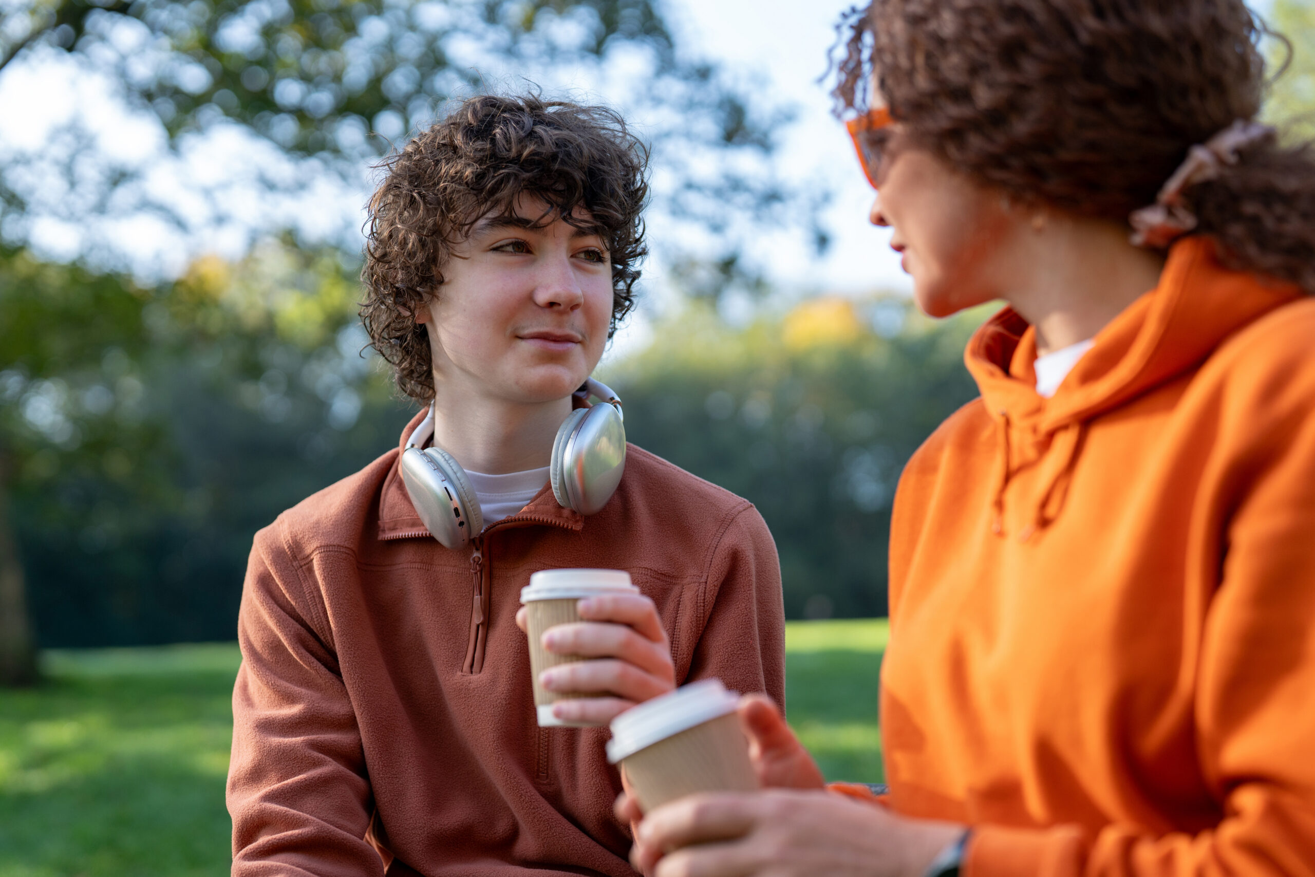 Two people sitting in a park drinking coffee.