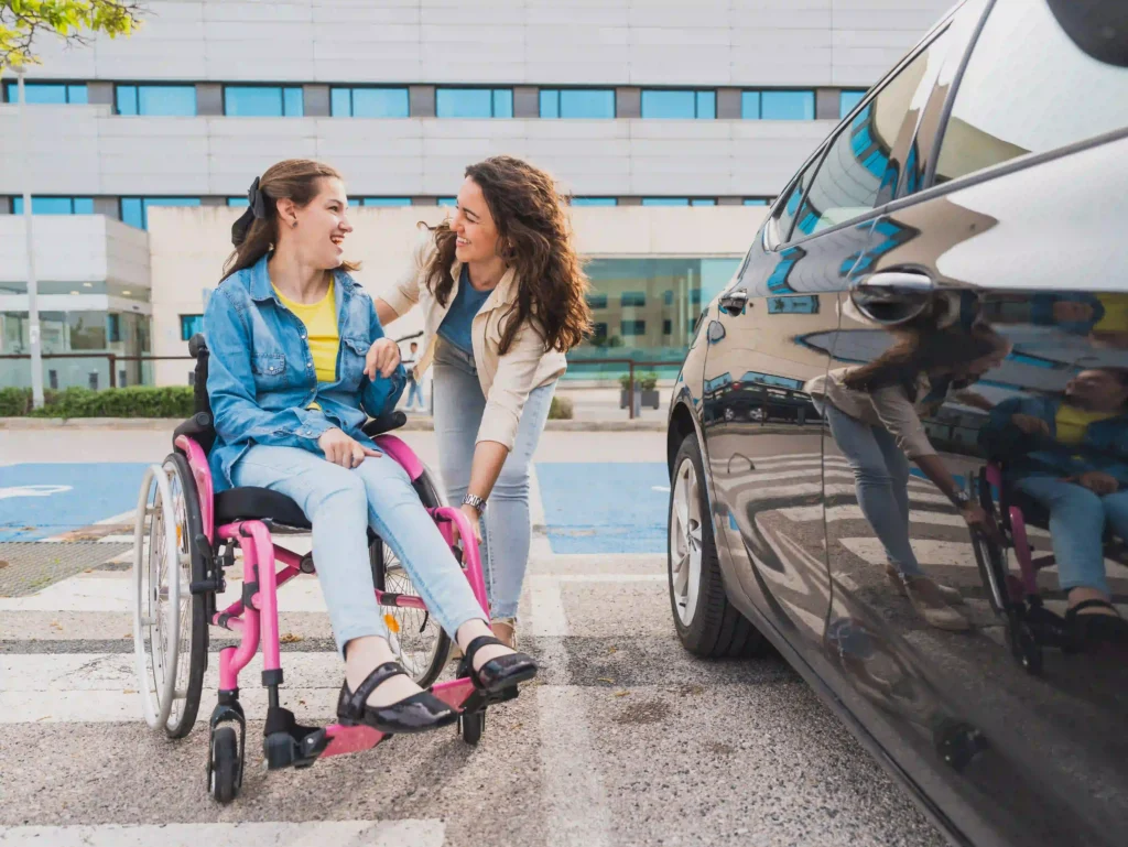 Woman in wheelchair with her support worker, getting out of the car in the car park.