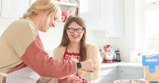 A mother and daughter in the kitchen cooking, both smiling.