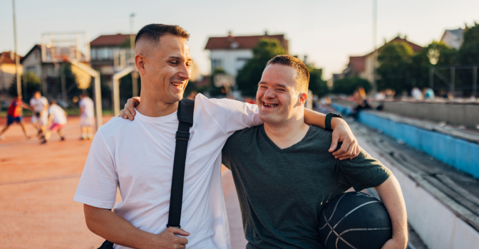 A young man with his support worker, with their arms around each other, both smiling
