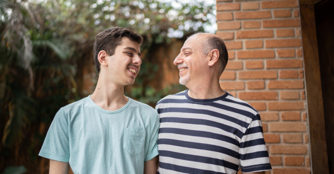 Young man with his father, standing and looking at each other, smiling