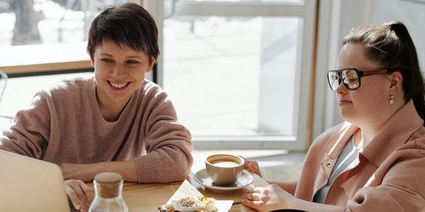 Support worker and client in a cafe looking at a laptop computer
