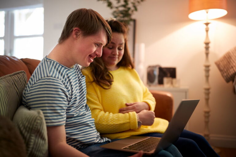 A young man and woman sitting on a sofa looking at a laptop computer