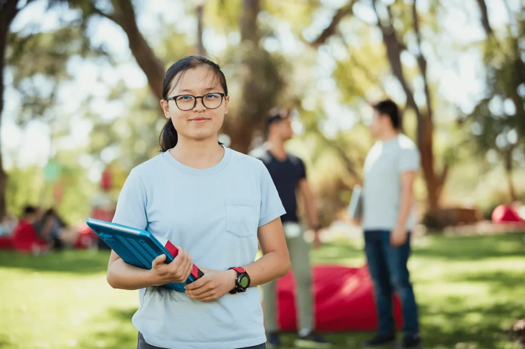 A young woman on campus holding a book and laptop computer