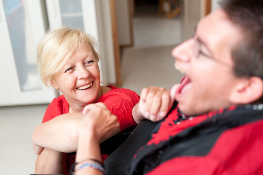 A man in a wheelchair with his carer beside him, both smiling