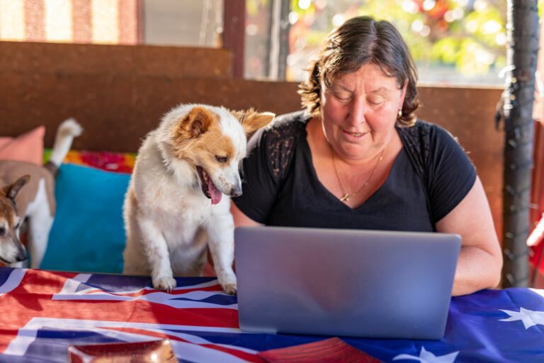 A woman working on a laptop computer with her dog by her side