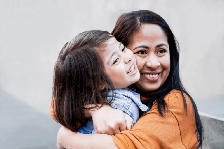 Mum cuddling her young daughter, both smiling