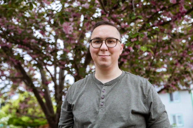 Man standing outdoors behind a tree in residential neighborhood