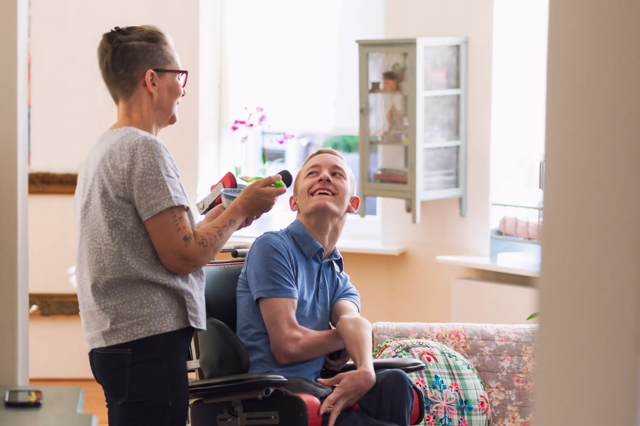 A young man in a wheelchair being fed by his carer