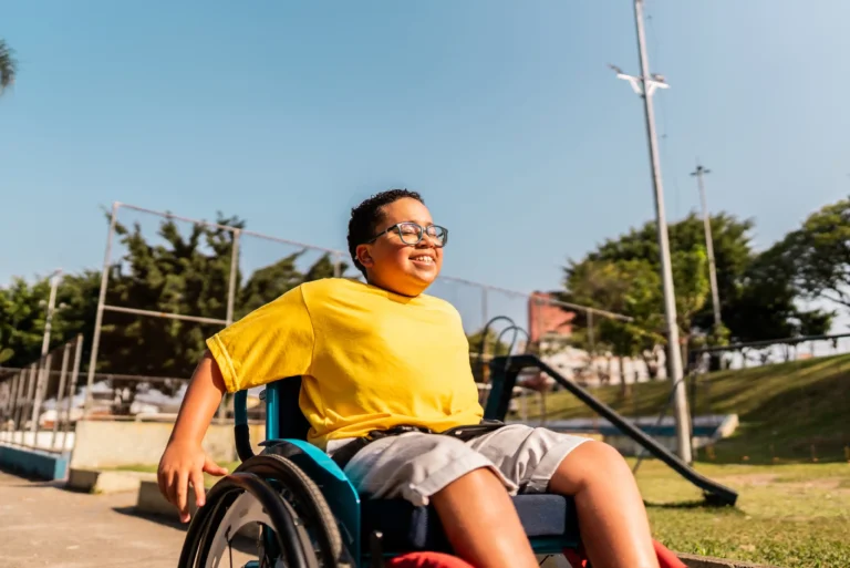 young boy in a wheelchair riding down a hill outside at a basketball court