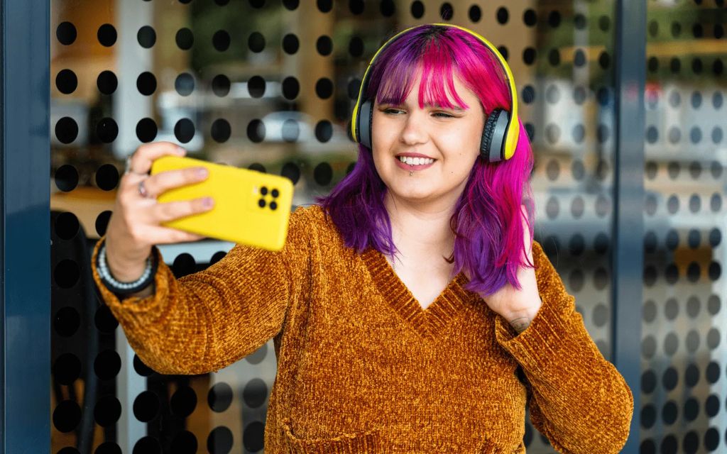 Girl with headphones on holding a smartphone out in front of her