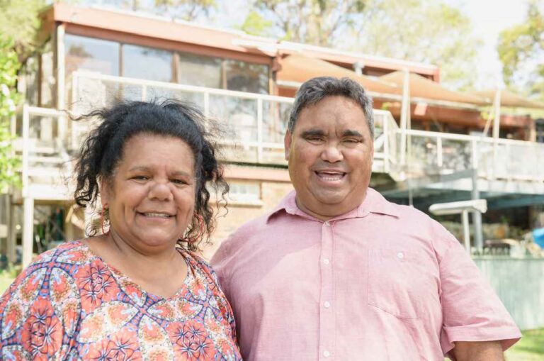 Two people standing in front of their house, smiling