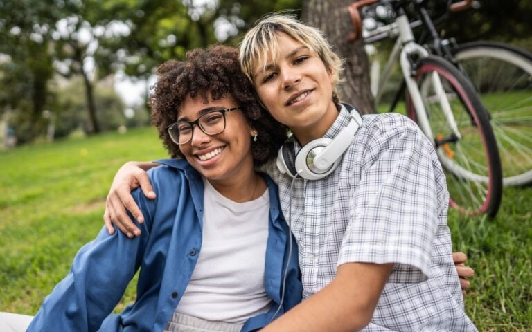 Two young people sitting on the grass one has an arm around the other