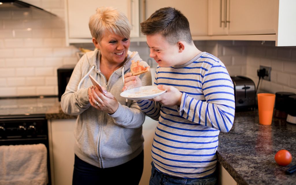 A woman is holding a smartphone showing the screen to a young man who is eating toast