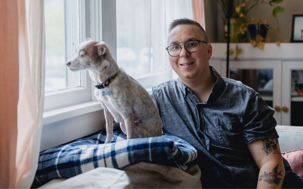 Smiling young man sitting at a window with his small dog.