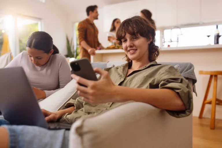 Young female sitting on couch looking at mobile device, surrounded by roomates