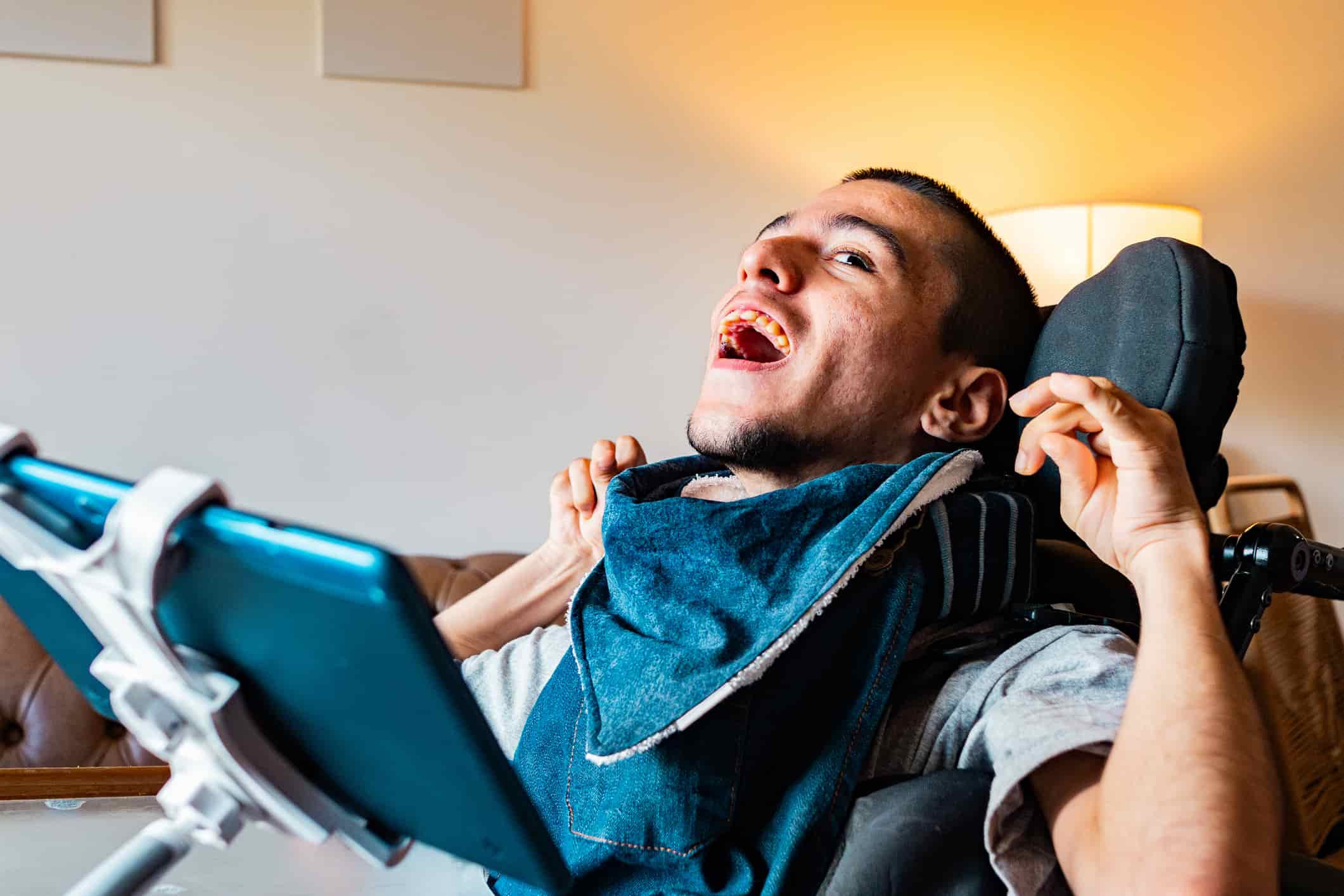 Smiling person using a wheelchair at home, with a mounted communication device positioned in front of them.