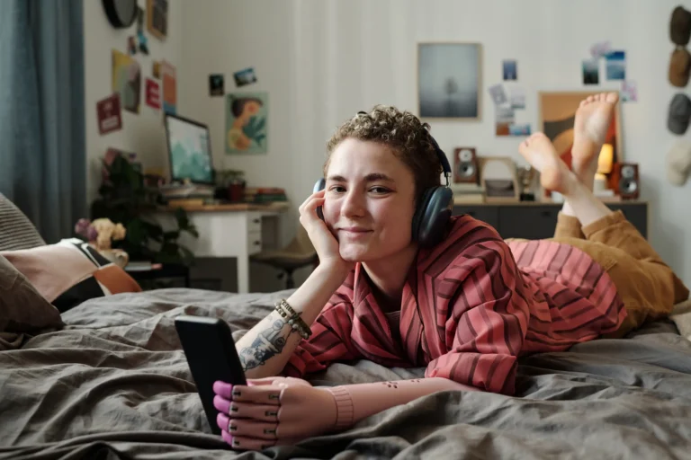Young adult listening to music on headphones while laying on bed.