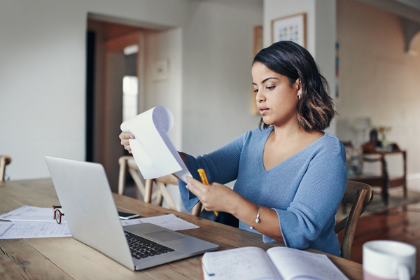 woman sitting doing paperwork at dining table with laptop open