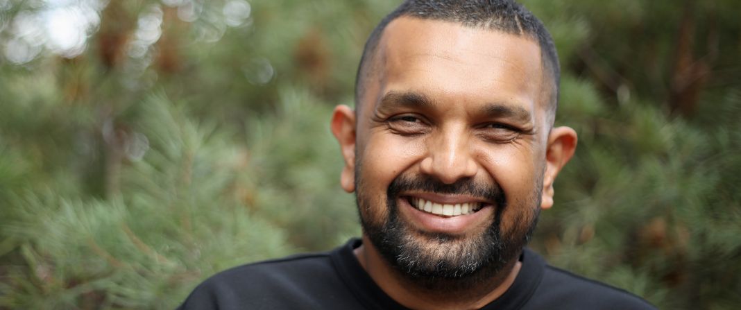 Dr Dinesh Palipana smiling at the camera with foliage behind him.