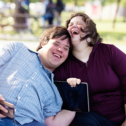 Man and a woman sitting on a park bench laughing