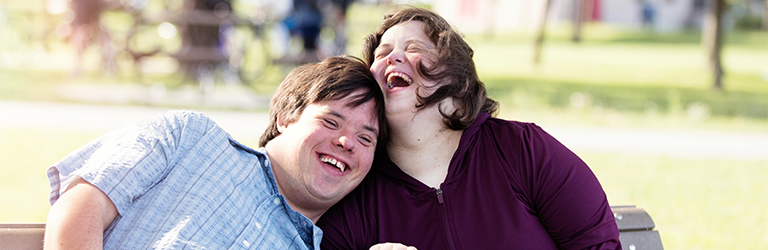 Man and a woman sitting on a park bench laughing