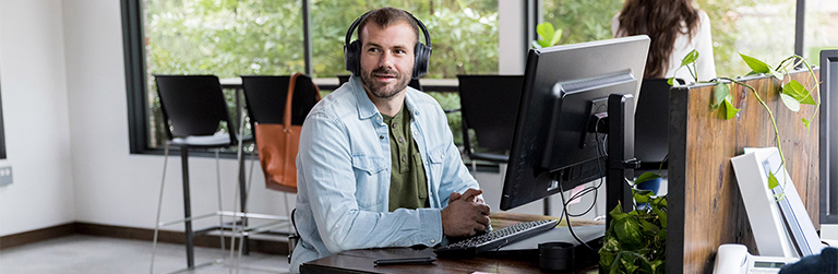 Man in a wheelchair at his office desk wearing headphones