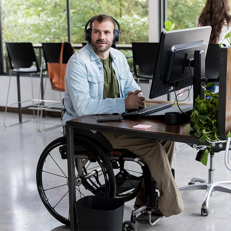 Man in a wheelchair at his office desk wearing headphones