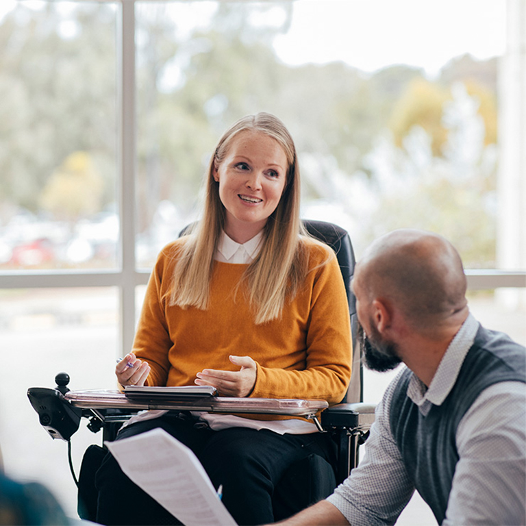 Woman in a wheel chair talking to a group in a meeting room