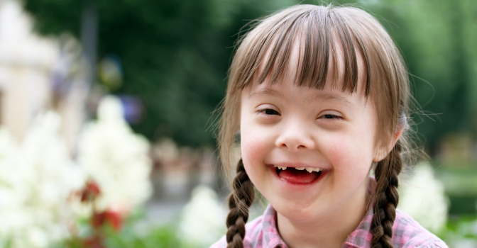 Young girl with disability smiling at the camera, outside.