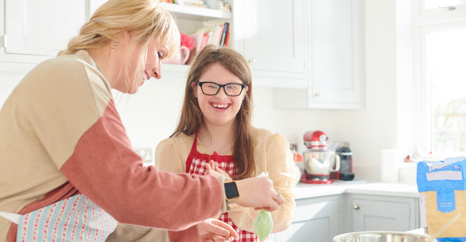 Young person with disability cooking in the kitchen, assisted by a carer.