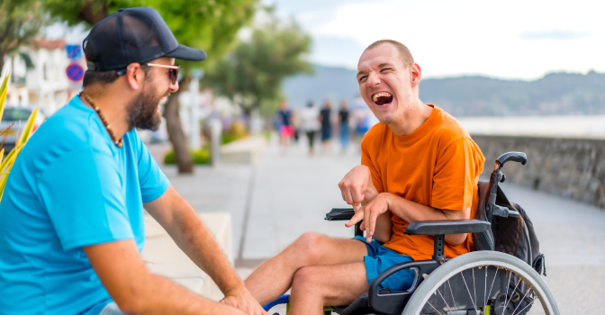 Young man with disability outside laughing with a friend sitting down.