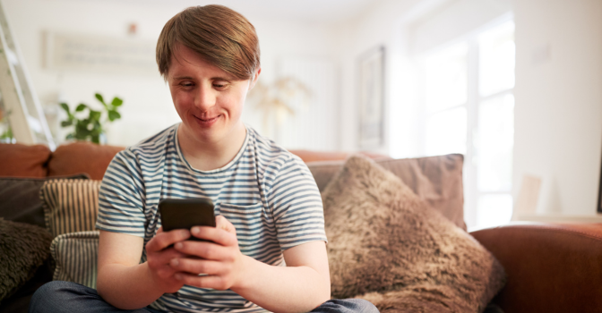 Young person with disability sitting on a couch using their mobile phone.