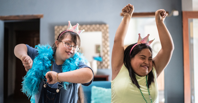 Two young girls with disability, dancing in a room.
