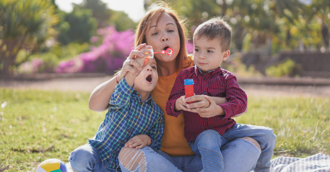 Mother with two children, sitting in a park blowing bubbles.