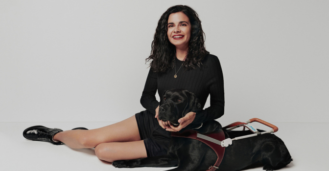 Aria Mia Loberti sitting with her guide dog, with a white background behind them.