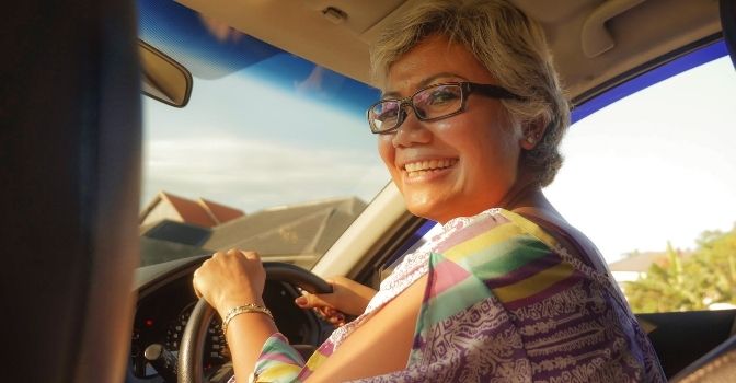 A woman is driving her car and smiilng.