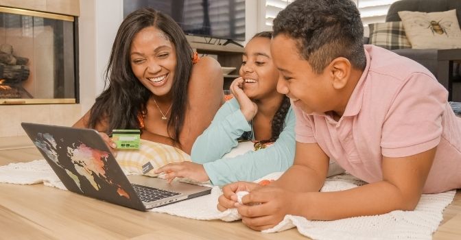 A mother and her two children are shopping online together on a laptop.