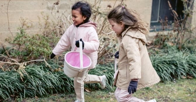 Two girls are smiling and running through a garden with easter baskets.
