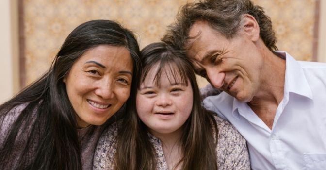 A family of a mum, dad and daughter have their heads together and are all smiling.