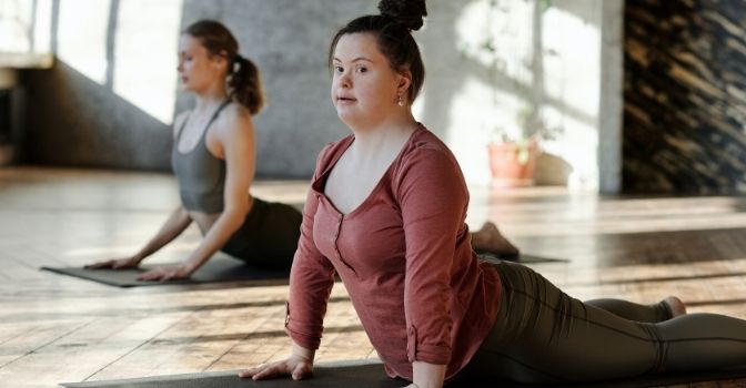 Two women are doing yoga stretches in a sun filled studio.