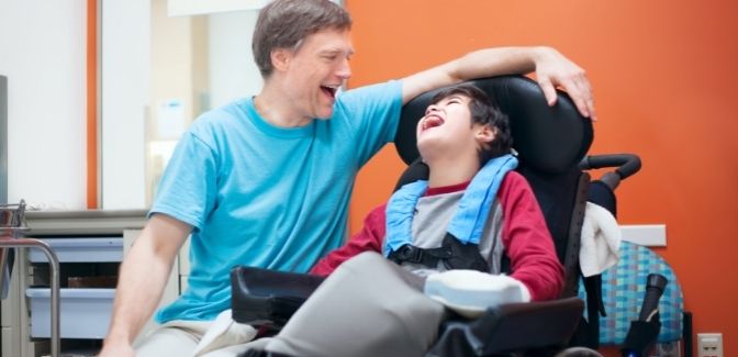 A boy is laughing and smiling at his carer while seated next to each other.
