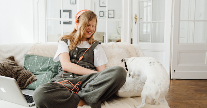 A woman sits on a lounge relaxing with her pink headphones anda white dog.